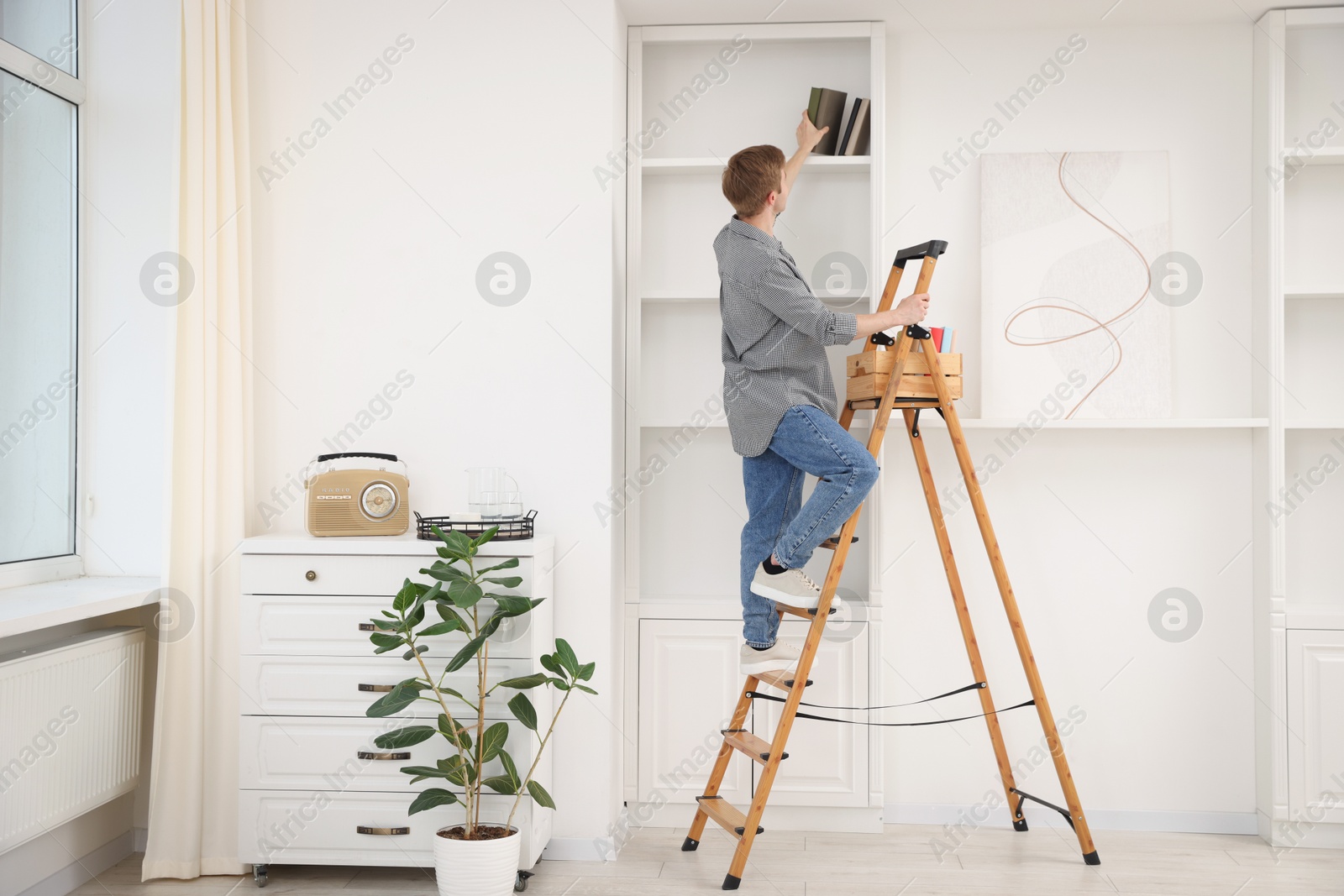 Man putting books on shelves using ladder at home Photo of Man putting books on shelves using ladder at home