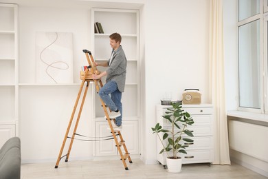 Photo of Man putting books on shelves using ladder at home