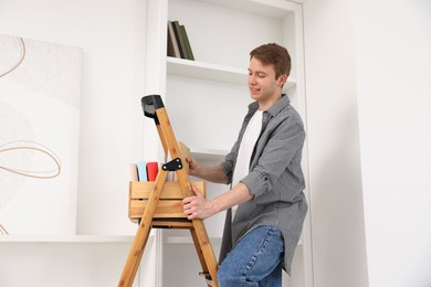Photo of Man putting books on shelves using ladder at home