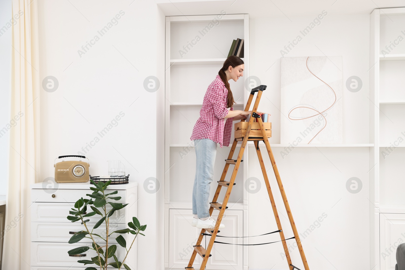 Woman putting books on shelves using ladder at home Photo of Woman putting books on shelves using ladder at home