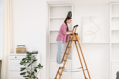 Photo of Woman putting books on shelves using ladder at home