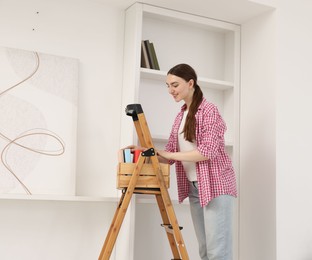 Photo of Woman putting books on shelves using ladder at home