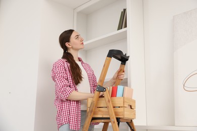 Photo of Woman putting books on shelves using ladder at home