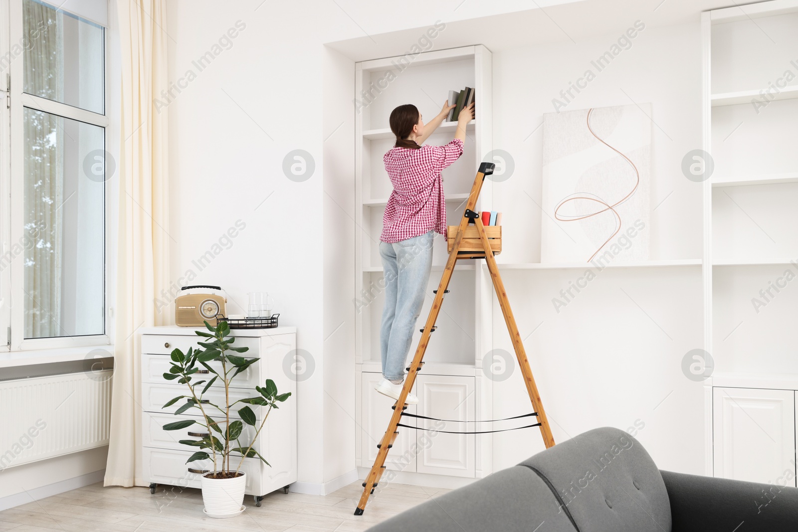 Woman putting books on shelves using ladder at home Photo of Woman putting books on shelves using ladder at home