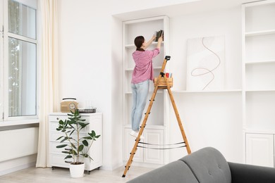 Photo of Woman putting books on shelves using ladder at home