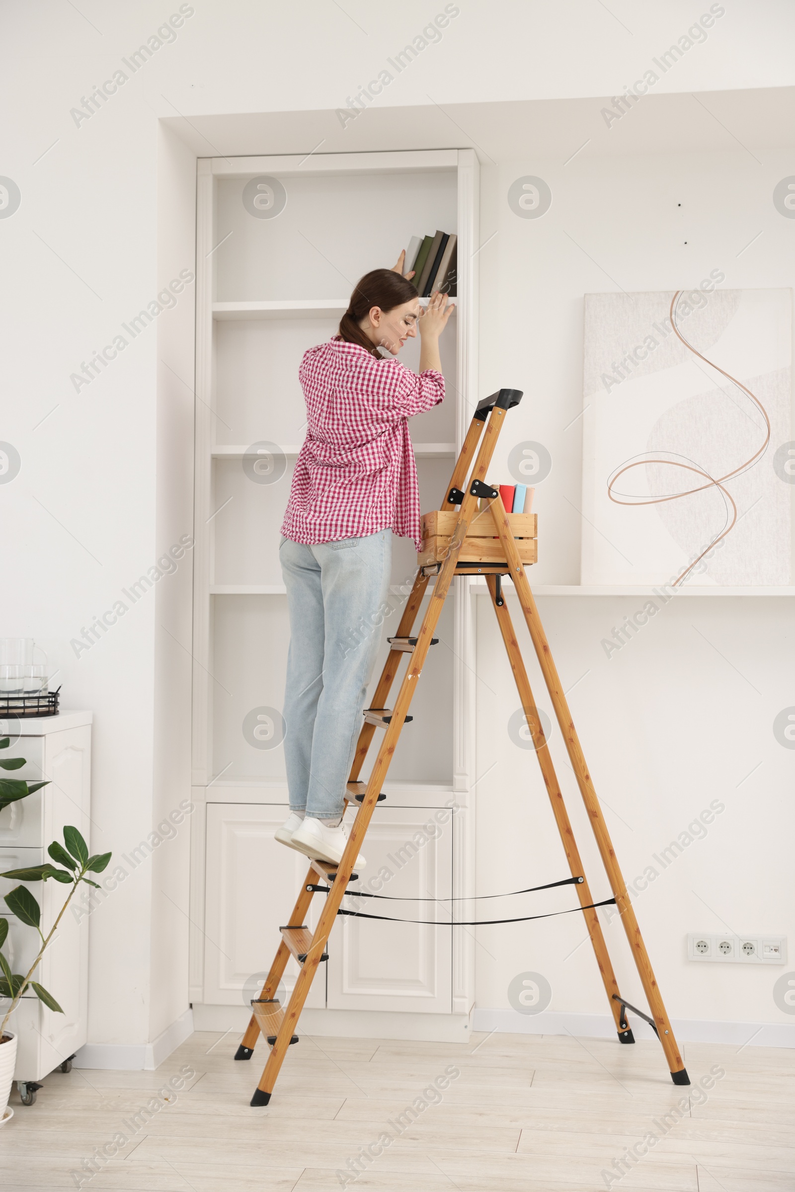 Woman putting books on shelves using ladder at home Photo of Woman putting books on shelves using ladder at home