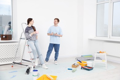 Photo of Couple with cups of coffee having break during renovation at home