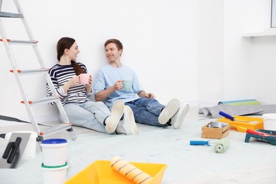 Photo of Couple with cups of coffee having break during renovation at home