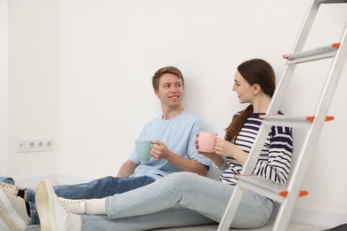 Photo of Couple with cups of coffee having break during renovation at home