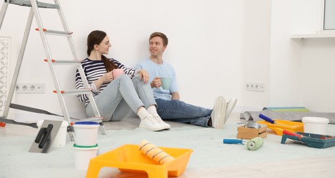 Photo of Couple with cups of coffee having break during renovation at home