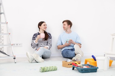 Photo of Couple with cups of coffee having break during renovation at home