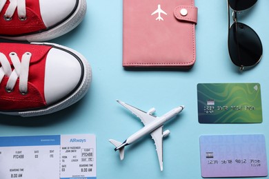 Photo of Airplane model, flight ticket, passport, credit cards, sunglasses and sneakers on light blue background, flat lay