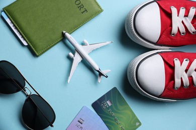 Photo of Airplane model, passport, credit cards, sunglasses and sneakers on light blue background, flat lay