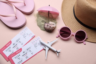 Photo of Flight tickets, airplane model, sand and beach accessories on beige background, flat lay
