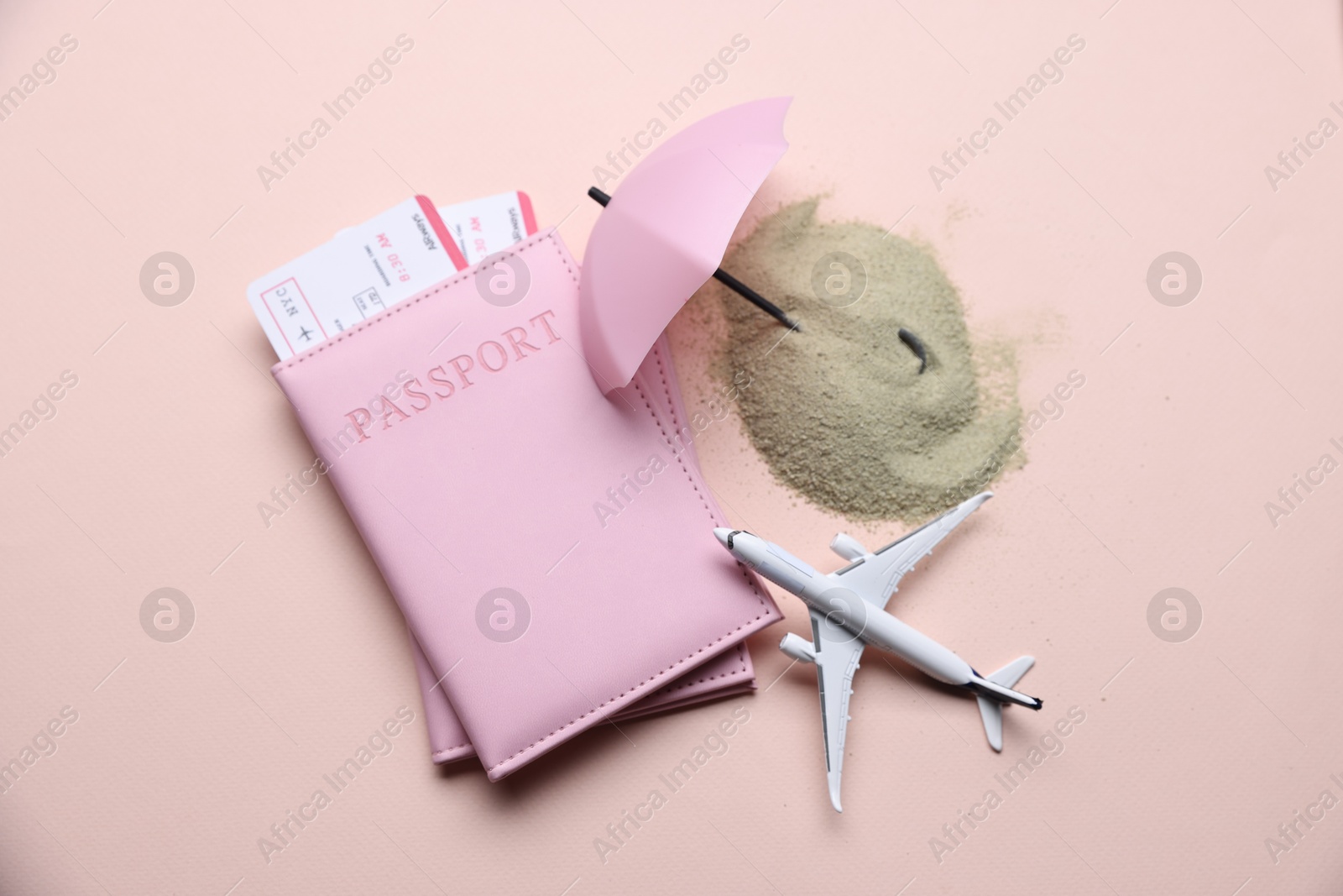 Photo of Airplane model, passports, flight tickets, sand and small umbrella on beige background, flat lay