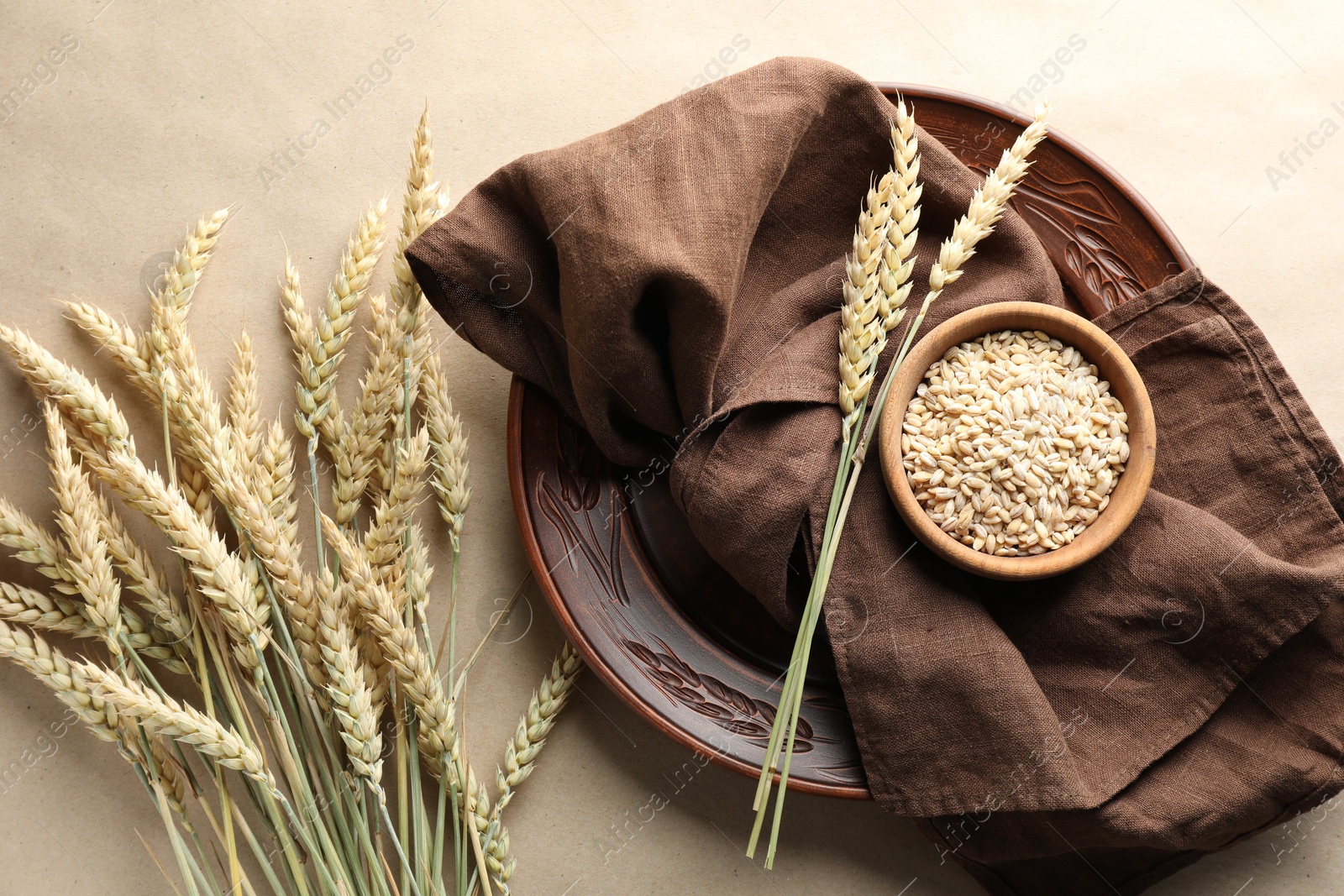 Photo of Many wheat spikes, plate, napkin and seeds on paper background, flat lay