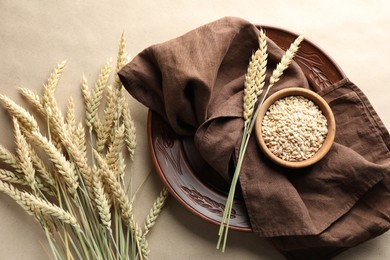 Photo of Many wheat spikes, plate, napkin and seeds on paper background, flat lay