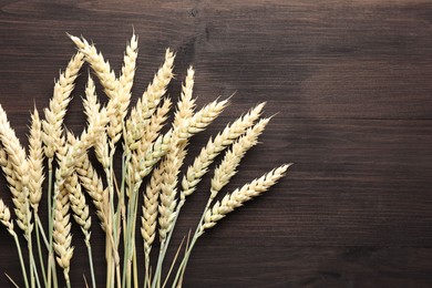 Photo of Many wheat spikes on wooden table, flat lay. Space for text