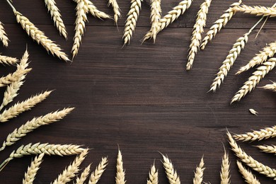 Photo of Frame of wheat spikes on wooden table, flat lay. Space for text