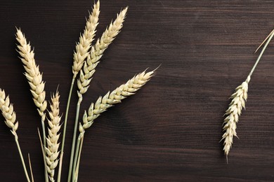 Photo of Many wheat spikes on dark wooden table, flat lay
