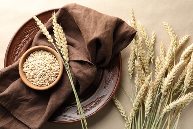Photo of Many wheat spikes, plate, napkin and seeds on paper background, flat lay