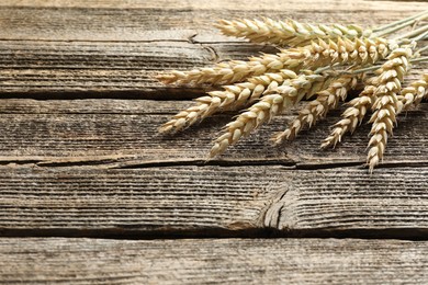 Photo of Many wheat spikes on wooden table, closeup. Space for text
