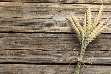 Photo of Bunch of wheat spikes on wooden table, top view. Space for text