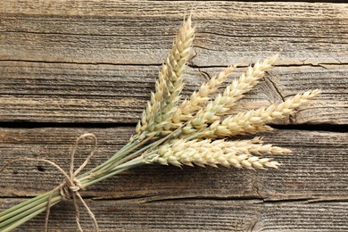 Photo of Bunch of wheat spikes on wooden table, top view