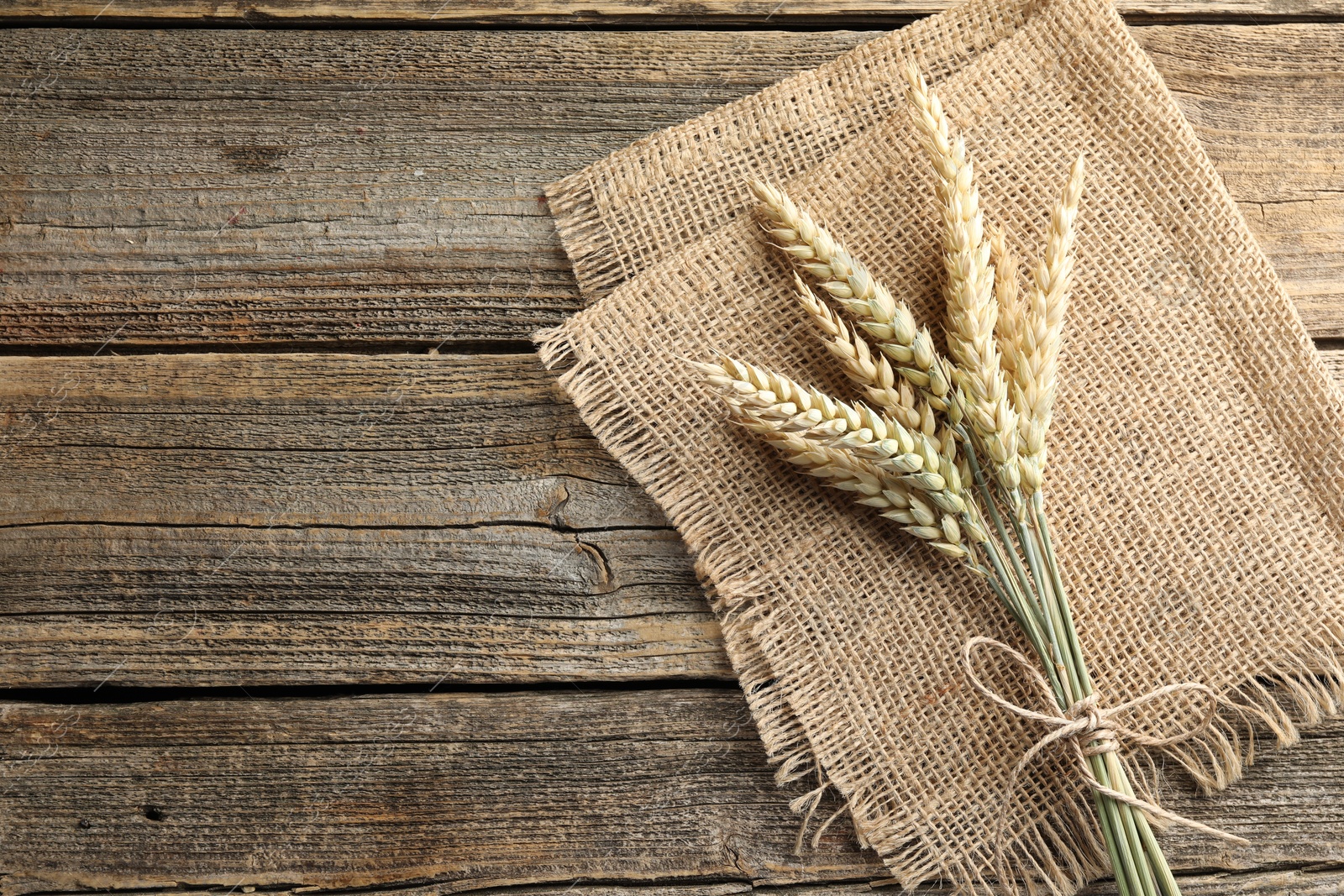 Photo of Bunch of wheat spikes on wooden table, top view. Space for text
