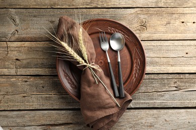 Photo of Wheat spikes, plate and cutlery on wooden table, top view