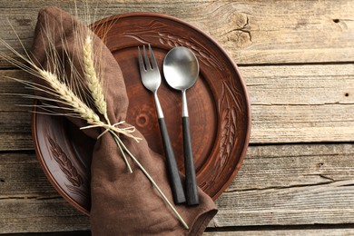 Photo of Wheat spikes, plate and cutlery on wooden table, top view. Space for text