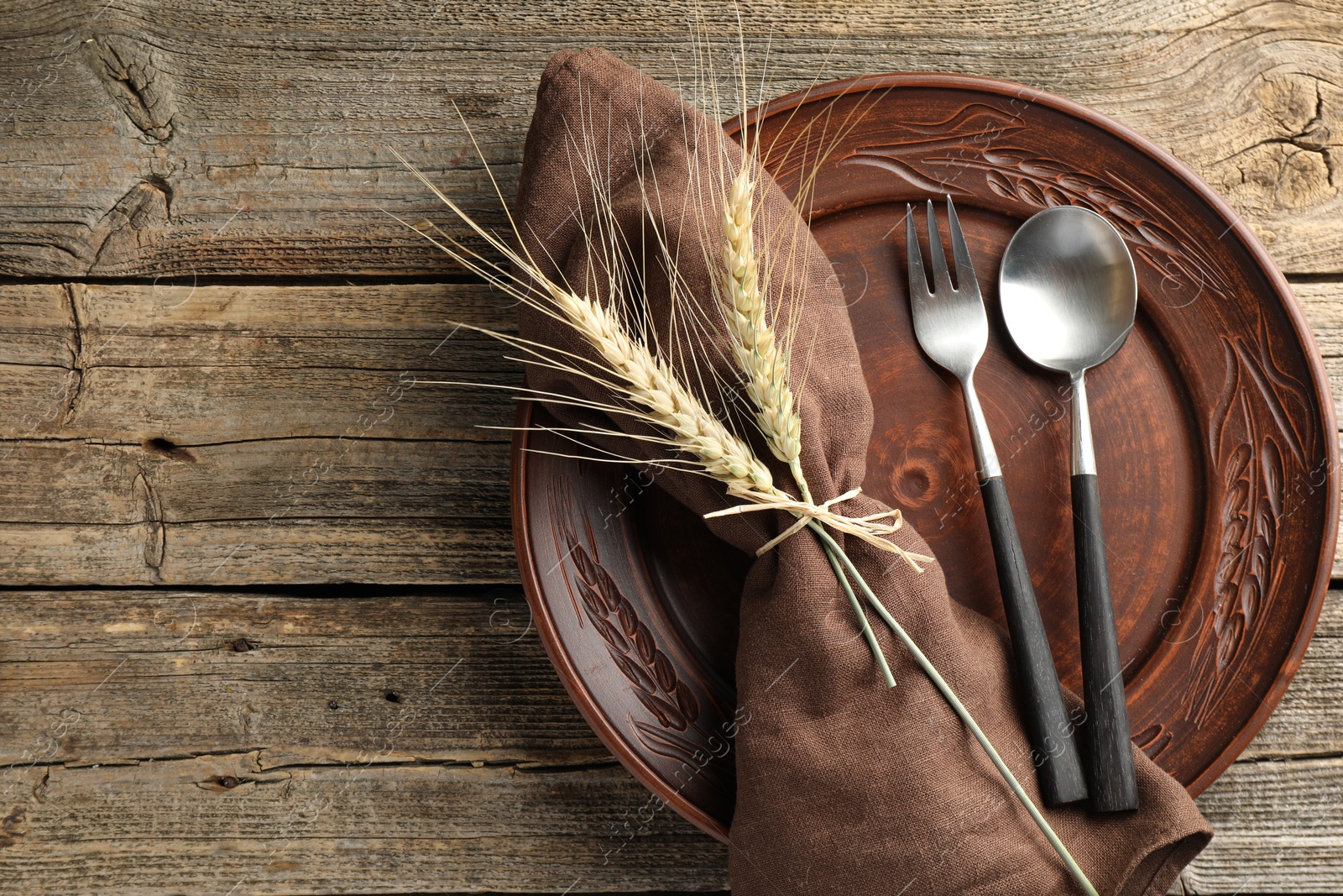 Photo of Wheat spikes, plate and cutlery on wooden table, top view. Space for text