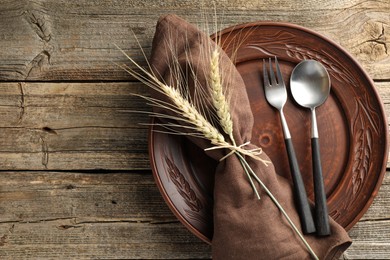 Photo of Wheat spikes, plate and cutlery on wooden table, top view. Space for text