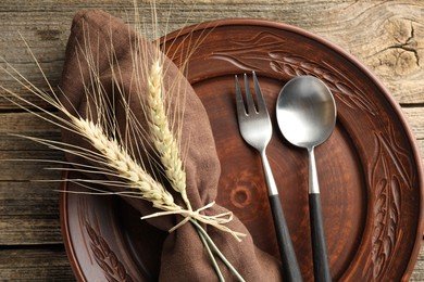 Photo of Wheat spikes, plate and cutlery on wooden table, top view