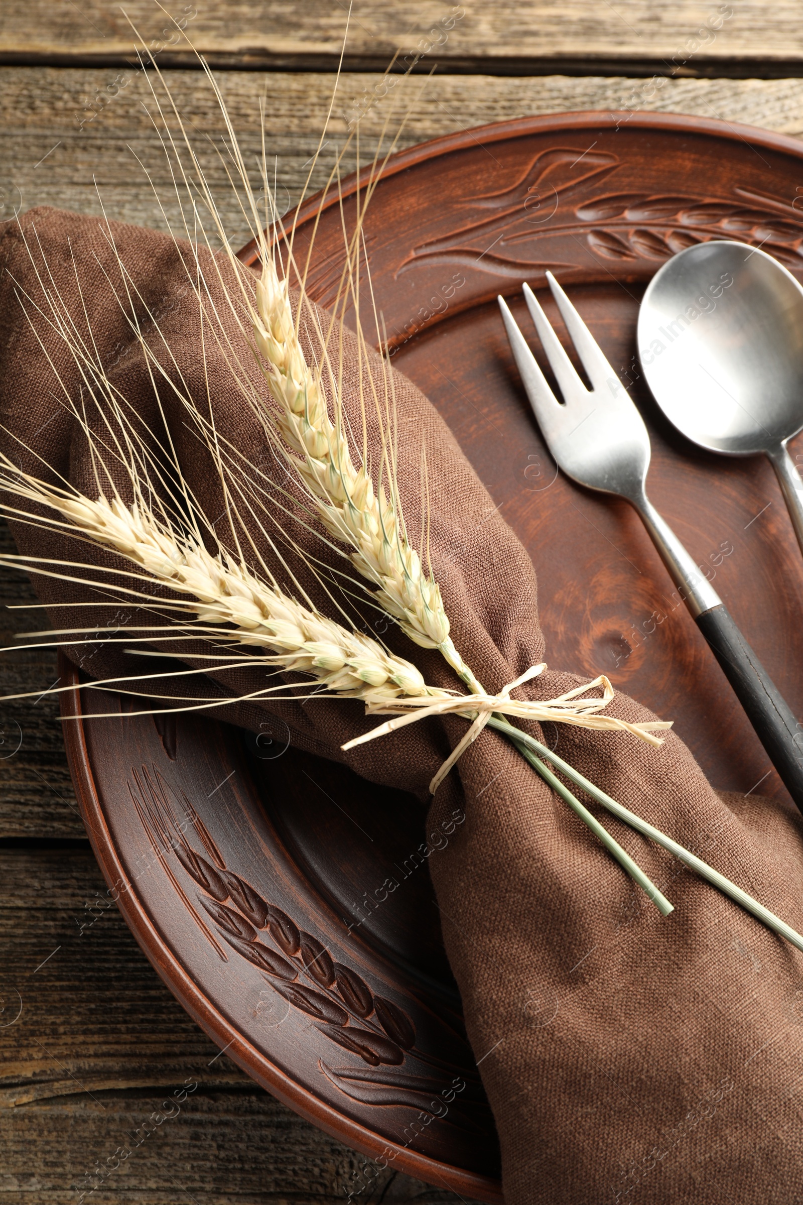 Photo of Wheat spikes, plate and cutlery on wooden table, top view