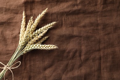 Photo of Bunch of wheat spikes on brown cloth, top view. Space for text