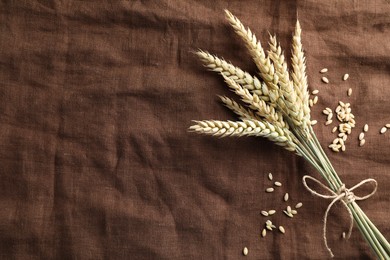 Photo of Bunch of wheat spikes and grains on brown cloth, flat lay. Space for text