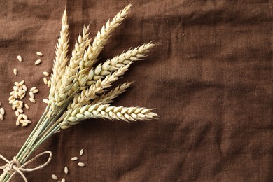 Photo of Bunch of wheat spikes and grains on brown cloth, flat lay. Space for text