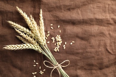 Photo of Bunch of wheat spikes and grains on brown cloth, flat lay. Space for text