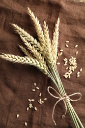 Photo of Bunch of wheat spikes and grains on brown cloth, flat lay