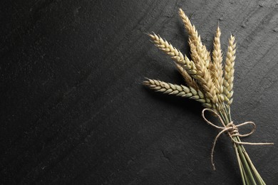 Photo of Bunch of wheat spikes on black table, top view. Space for text