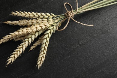 Photo of Bunch of wheat spikes on black table, top view. Space for text