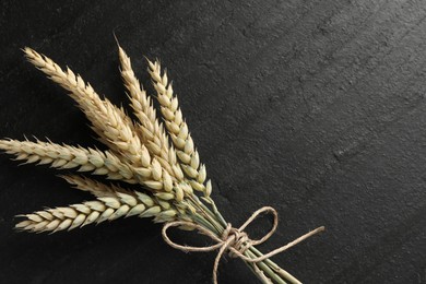Photo of Bunch of wheat spikes on black table, top view. Space for text