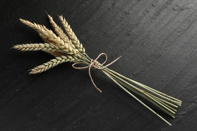 Photo of Bunch of wheat spikes on black table, top view