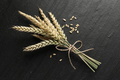 Photo of Bunch of wheat spikes and grains on black table, flat lay