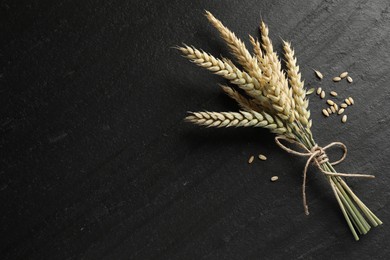 Photo of Bunch of wheat spikes and grains on black table, flat lay. Space for text