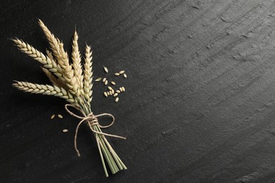 Photo of Bunch of wheat spikes and grains on black table, flat lay. Space for text