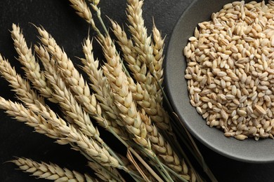 Photo of Many wheat spikes and grains on black table, flat lay