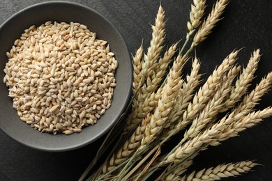 Photo of Many wheat spikes and grains on black table, flat lay