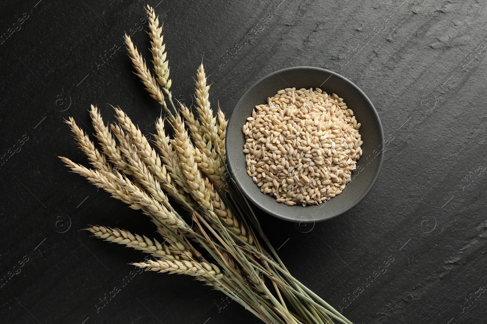 Photo of Many wheat spikes and grains on black table, flat lay